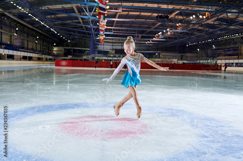 Full length portrait of talented little girl figure skating in indoor rink during performance in spotlight, copy space photo