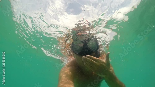 Diver man with snorkeling mask giving kisses, waves hand greetings and shows BON APETTITE hand sign underwater, gopro dome shot photo