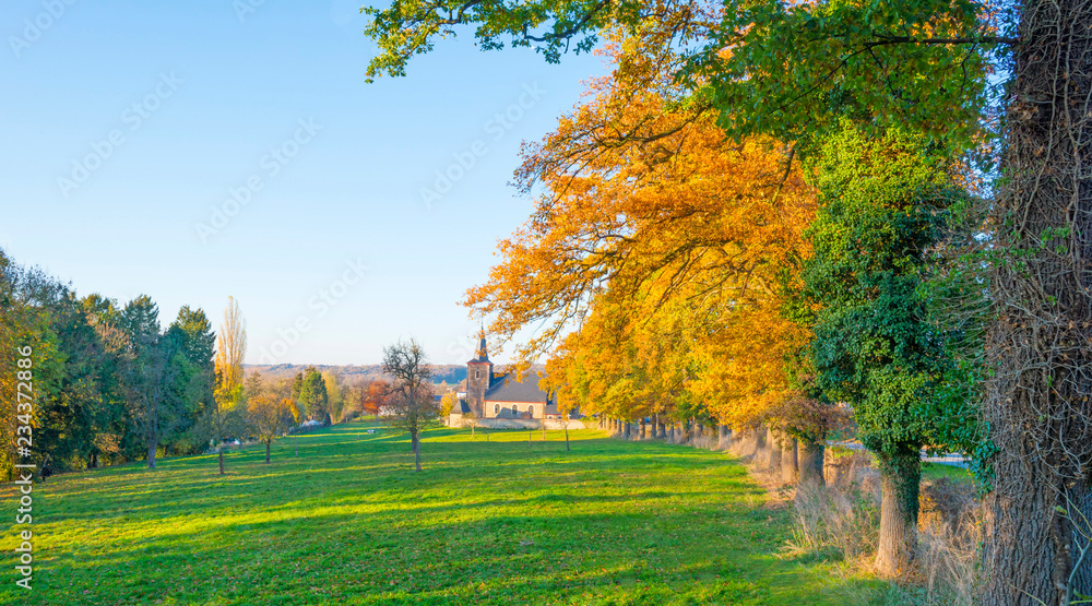Ancient church along trees below a blue sky in sunlight at fall
