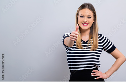 Young woman giving thumb up on a gray background