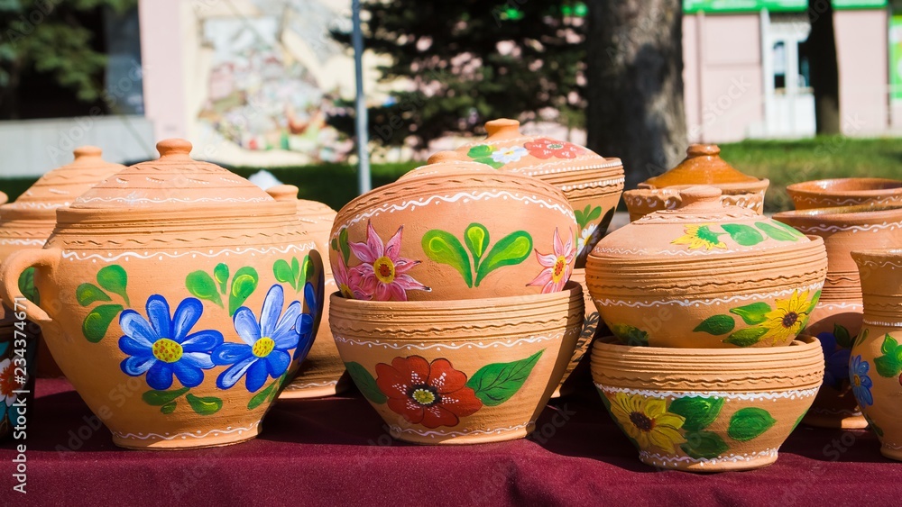 many handmade and handpainted ceramic clay jugs, pots with bright floral patterns in bright sunshine