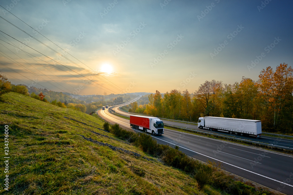 Trucks driving on the asphalt highway in autumn landscape at sunset