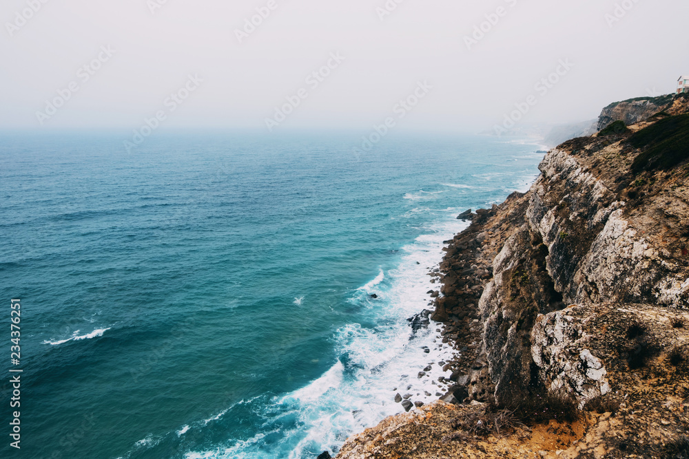 Ocean coast line cliff in a cloudy fogy day..Aerial view of waves breaking to the rocky shore of Atlantic ocean in Portugal.