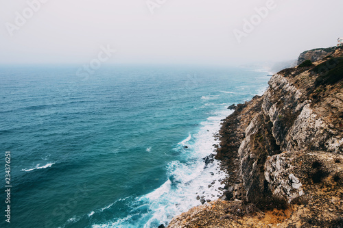 Ocean coast line cliff in a cloudy fogy day..Aerial view of waves breaking to the rocky shore of Atlantic ocean in Portugal.