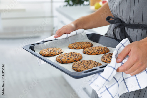Young man holding oven sheet with cookies in kitchen, closeup
