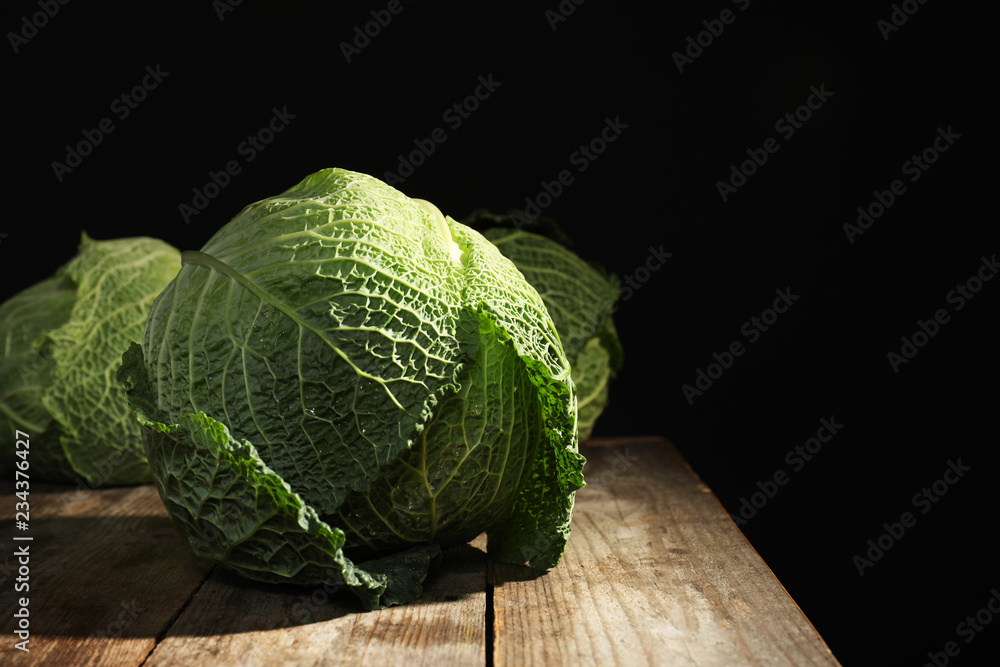 Fototapeta premium Savoy cabbage on wooden table against black background. Space for text