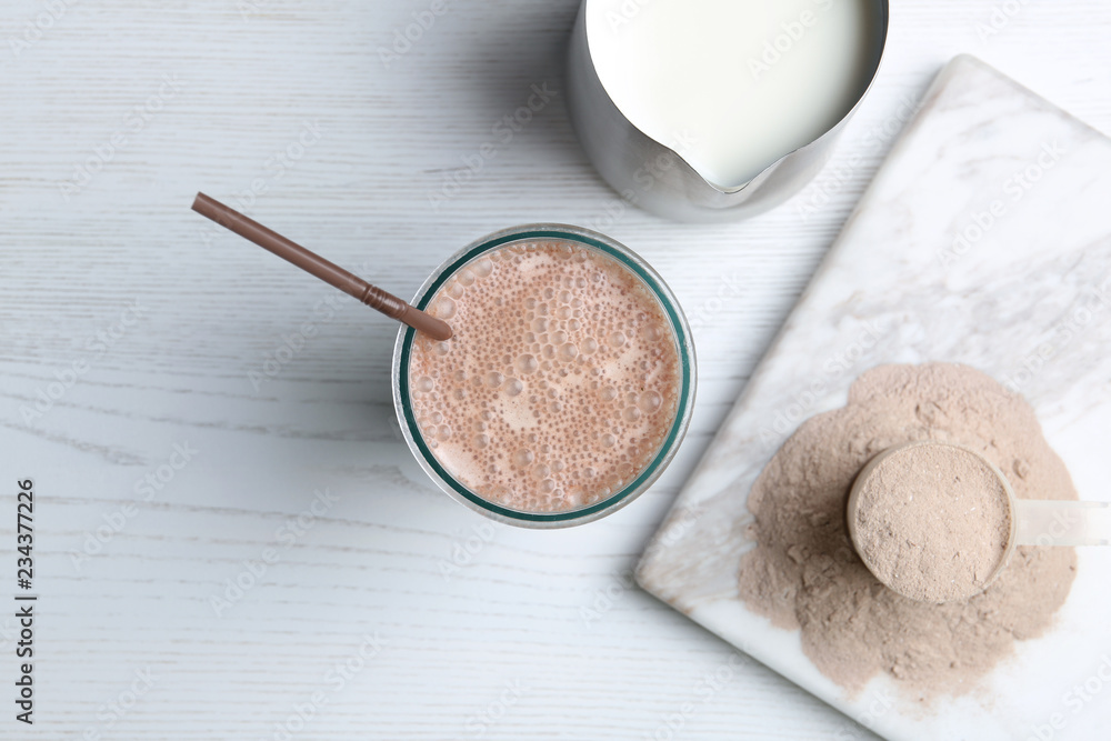 Glass with protein shake, jug of milk and powder on white wooden table, top view Glass with protein shake, jug of milk and powder on white wooden table, top view