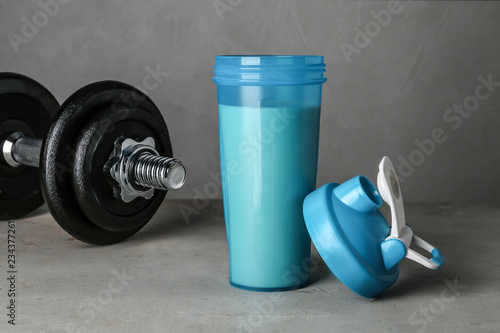 Bottle with protein shake and dumbbell on grey table