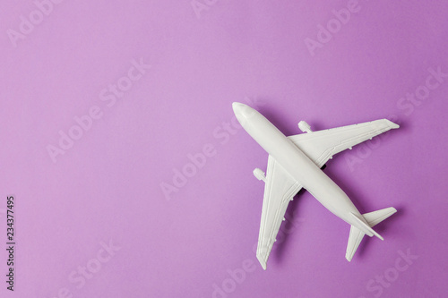 Simply flat lay design miniature toy model plane on violet purple pastel colorful paper trendy background. Travel by plane vacation summer weekend sea adventure trip journey ticket tour concept