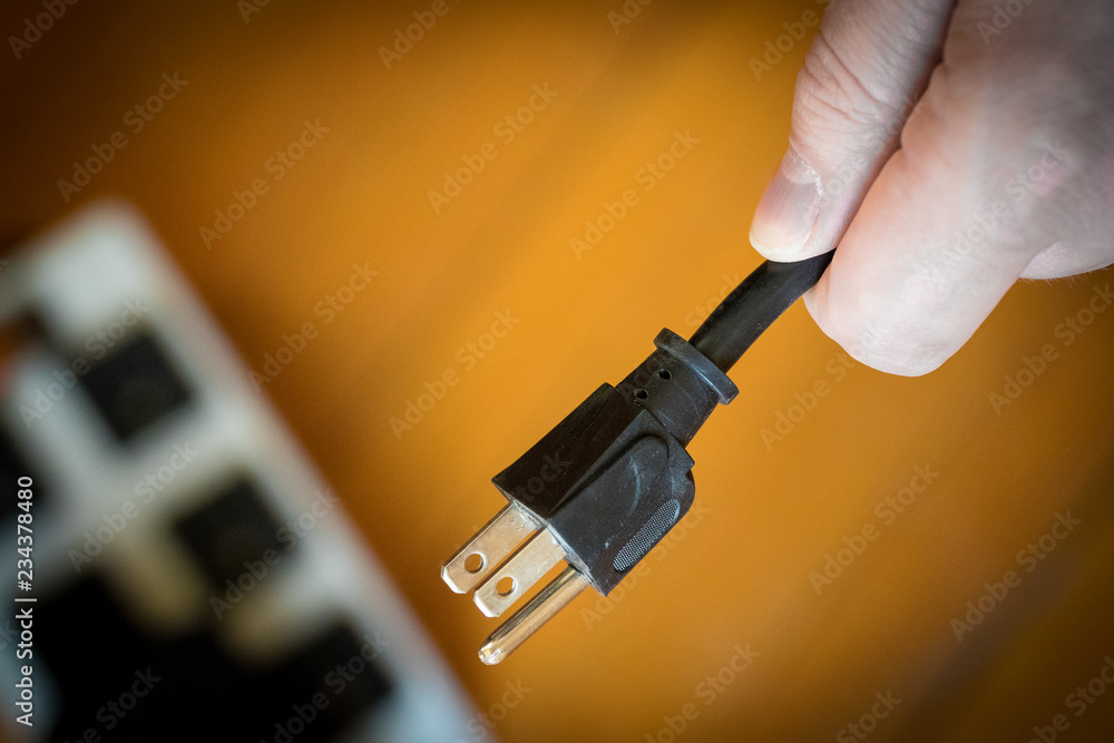 Grounded electric cable cord in hand, ready to plug or unplug from