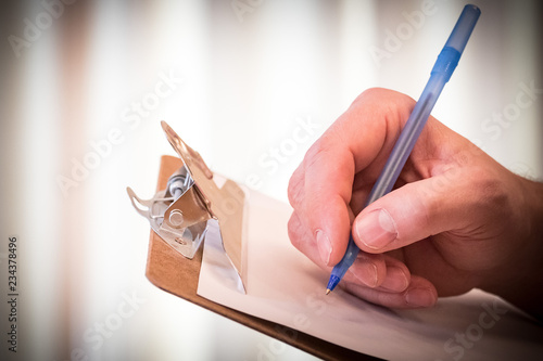 Man's hand puts pen to paper on a clipboard, to sign a form, make a list, or fill out information. photo