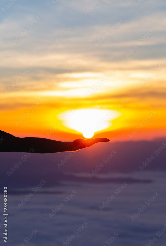 Silhouette of hand holding sun at winter morning sunrise