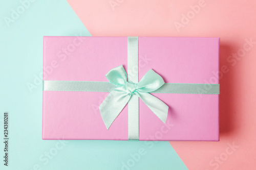 Small gift box wrapped pink and blue paper isolated on blue and pink pastel colorful trendy geometric background. Christmas New Year birthday valentine celebration present romantic concept photo