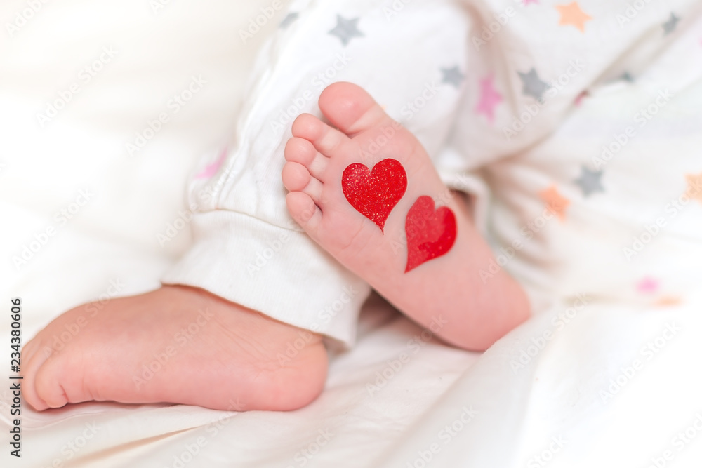 Baby foots with hearts on their feet. A newborn baby is lying on the bed. Baby foots with hearts on their feet. A newborn baby is lying on the bed.