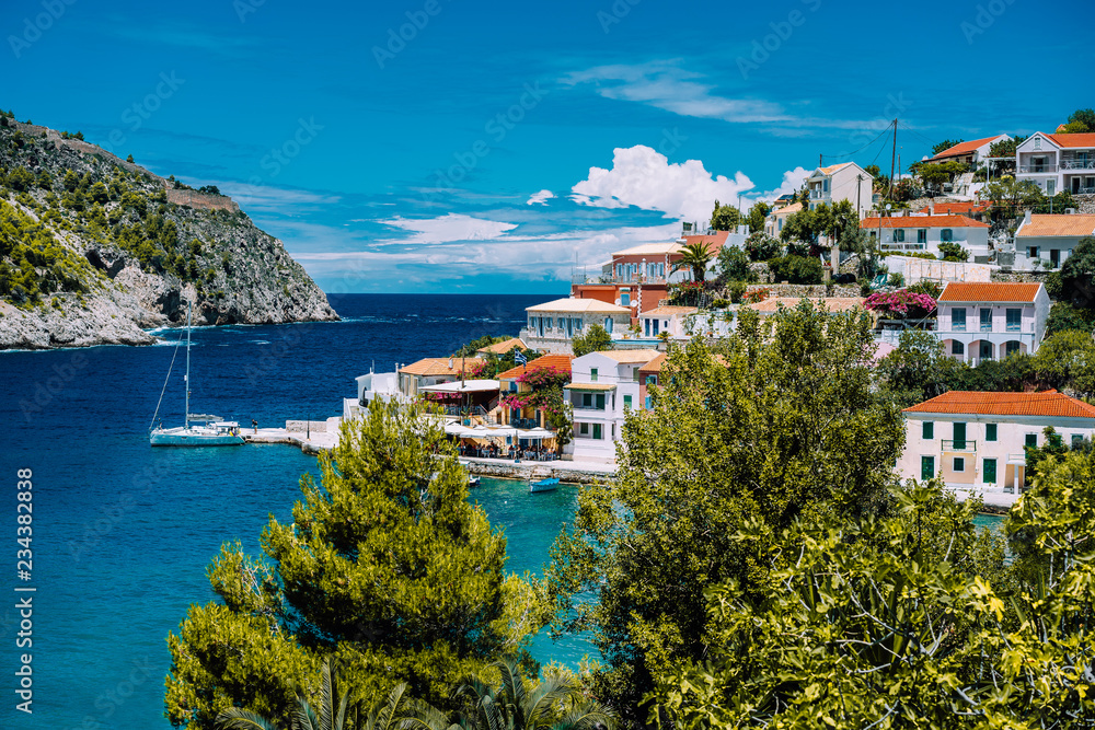 Assos village. Beautiful view to vivid colorful houses near blue turquoise colored transparent bay lagoon with yacht ship. Kefalonia, Greece
