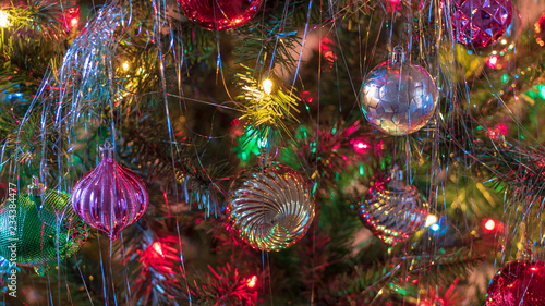 Brightly colored, cheery Christmas tree ornaments hung up with lights and tinsel