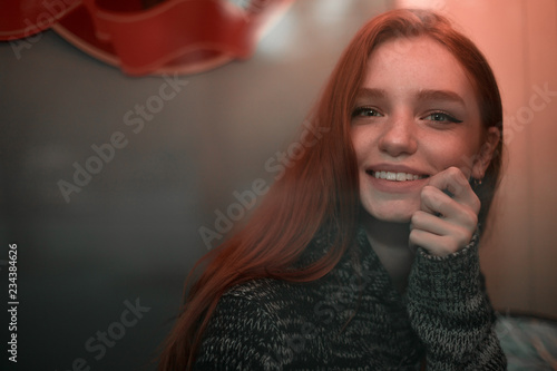 The portrait of a redhead smilling girl in gray sveater sitting in a cafe pleased