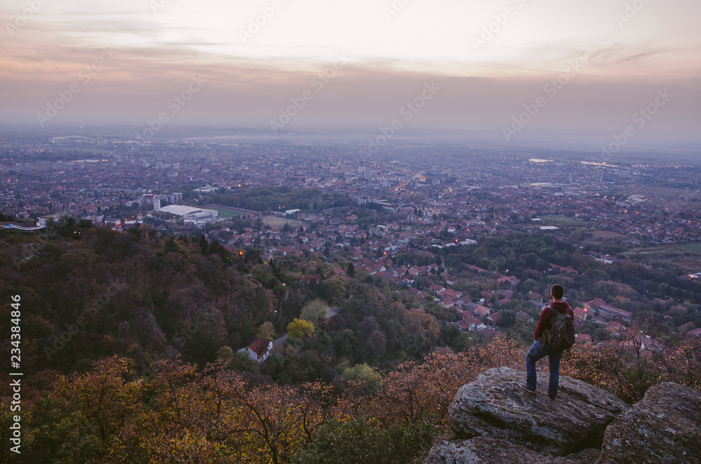 Hiker standing on the rock watching city at sunset