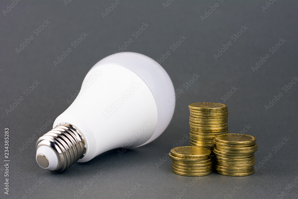 energy saving lamp and coins on gray background. using less energy reduces energy costs concept energy saving lamp and coins on gray background. using less energy reduces energy costs concept
