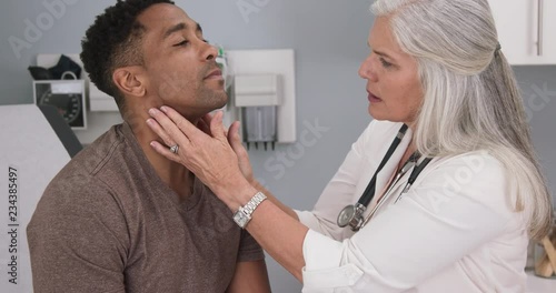 Close up of senior female doctor examining male patients neck. Portrait of attractive black male having doctor checkup at health clinic