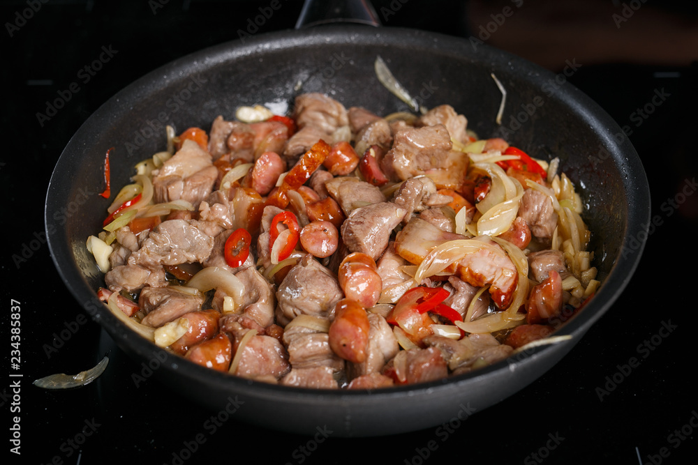 Frying pan with different kinds of meat, onions and chilli