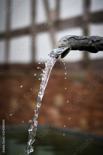 water flowing and splashing from old tap with timbered vintage house in the background © pixxelmixx