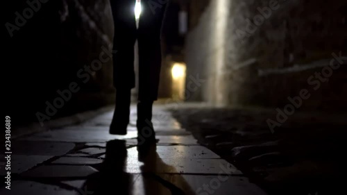 Cinematic treking of woman feet in boot walking on stone pavement in old alley dark street photo