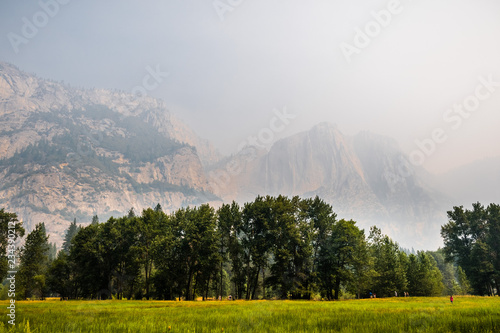 Landscape in Yosemite Valley; green meadow in the foreground; rock walls and Yosemite Upper Falls visible in the background through smoke from Ferguson Fire; Yosemite National Park, California photo