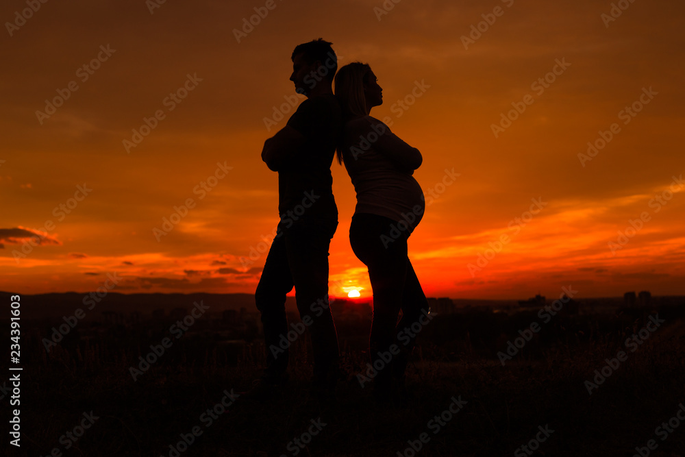 Silhouettes of husband and pregnant wife having conflict while they standing outdoor.