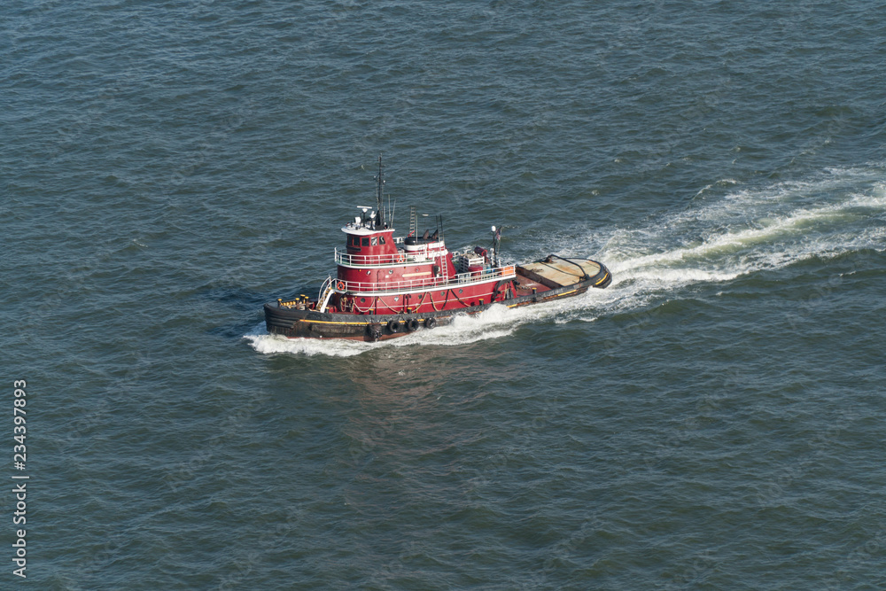 Aerial view of a New York City harbor tug boat sailing through water to assist large container and tank ships into port