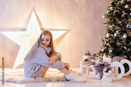 Beautiful young woman posing under Christmas tree in a holiday interior © Smile