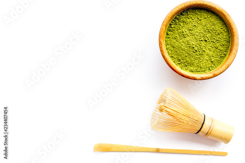 Matcha powder in bowl near specail stick and whisk on white background top view copy space