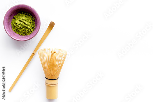 Matcha powder in bowl near specail stick and whisk on white background top view copy space