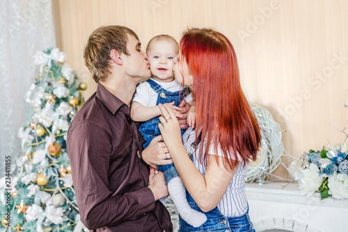 parents kissing baby next to Christmas tree