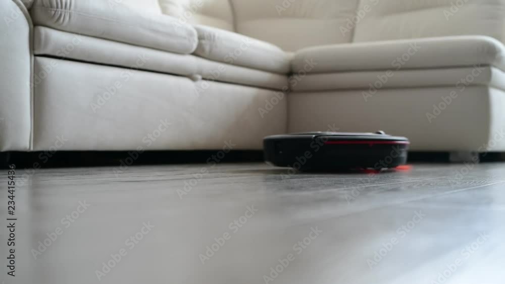 Robot vacuum cleaner collects dust in room near white sofa. Robot vacuum cleaner collects dust in room near white sofa.