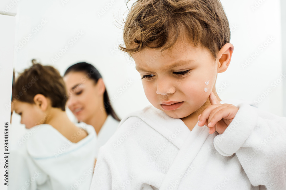confused toddler boy touching cheek with face cream confused toddler boy touching cheek with face cream