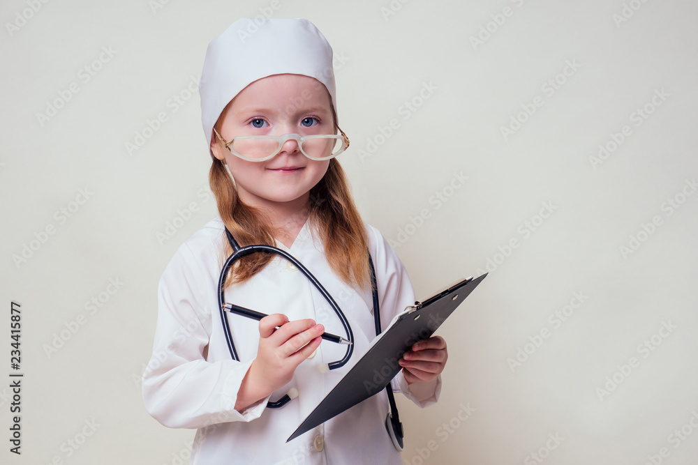 smiling little girl in doctor uniform with medical tools stethoscope writing something to clipboard on white background in studio copy space.future profession vocational guidance career smiling little girl in doctor uniform with medical tools stethoscope writing something to clipboard on white background in studio copy space.future profession vocational guidance career