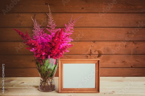 Wooden frame and beautiful astilbe flowers in glass vase on wooden table. View with copy space.