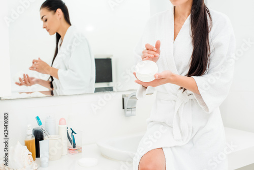 attractive woman sitting near sink with body cream in bathroom