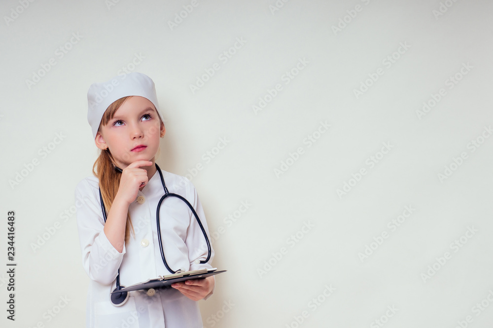 smiling little girl in doctor uniform with medical tools stethoscope writing something to clipboard on white background in studio copy space.future profession vocational guidance career smiling little girl in doctor uniform with medical tools stethoscope writing something to clipboard on white background in studio copy space.future profession vocational guidance career