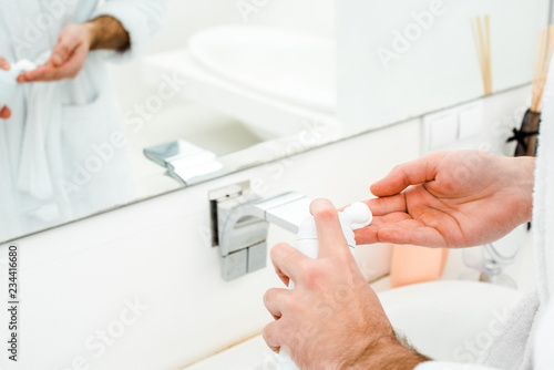 Male hands holding shaving foam in front of mirror in bathroom