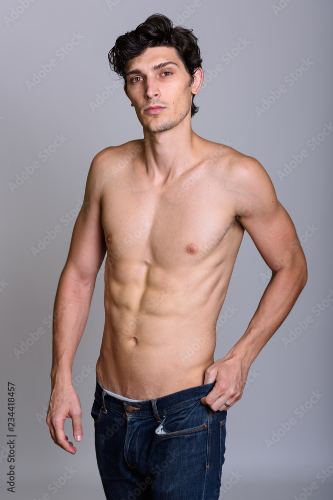 Studio shot of young handsome man posing while holding jeans shi