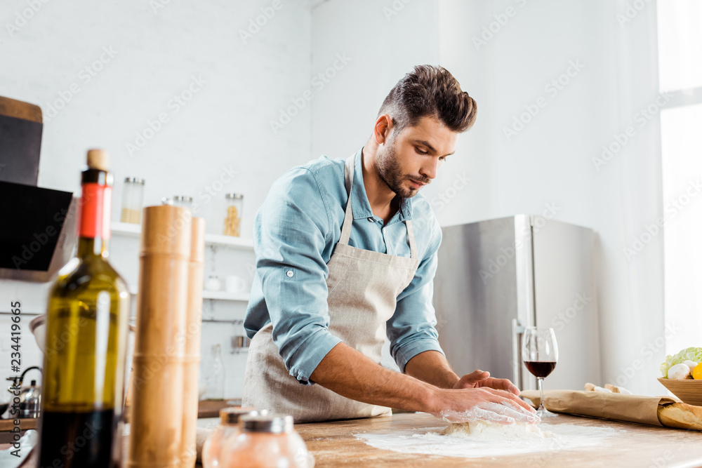 low angle view of focused young man in apron preparing dough in kitchen low angle view of focused young man in apron preparing dough in kitchen