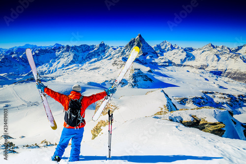 Man skiing on fresh powder snow. Ski in winter season, mountains and ski touring backcountry equipments on the top of snowy mountains in sunny day with Matterhorn in background, Zermatt in Swiss Alps.