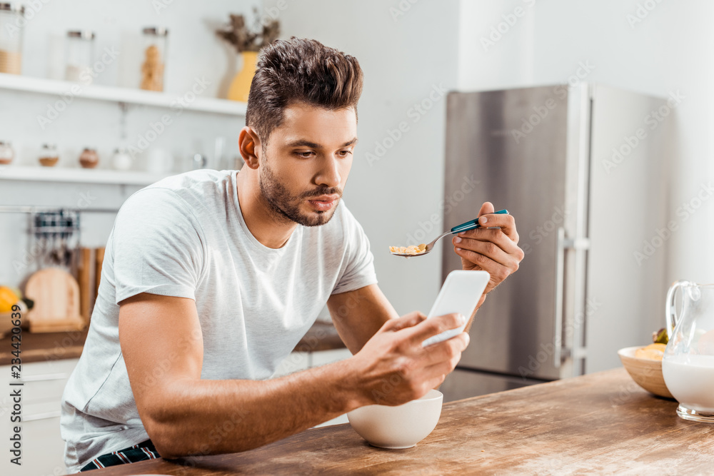 handsome young man using smartphone and having breakfast at home handsome young man using smartphone and having breakfast at home