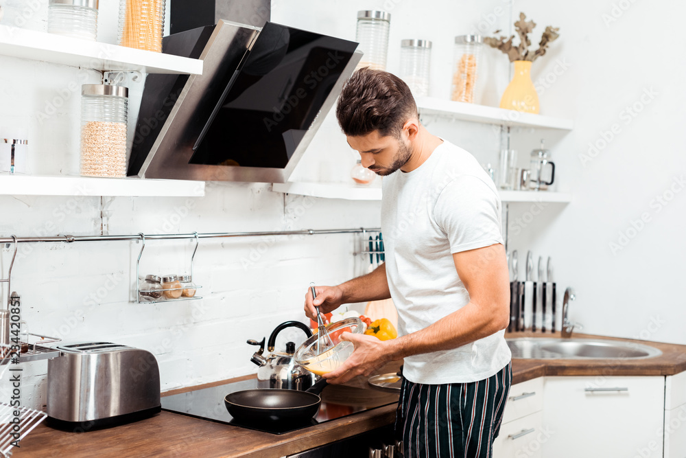 handsome young man in pajamas cooking omelette in frying pan at morning handsome young man in pajamas cooking omelette in frying pan at morning