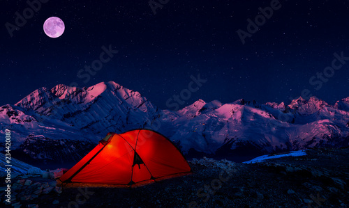 Night bivouac in Mountains, milion star hotel under night sky, red illuminated tent on pass in Alps.