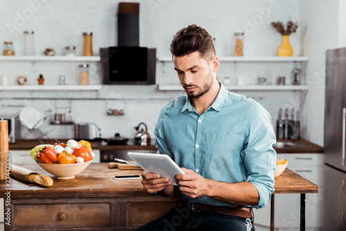 handsome young man using digital tablet while cooking in kitchen