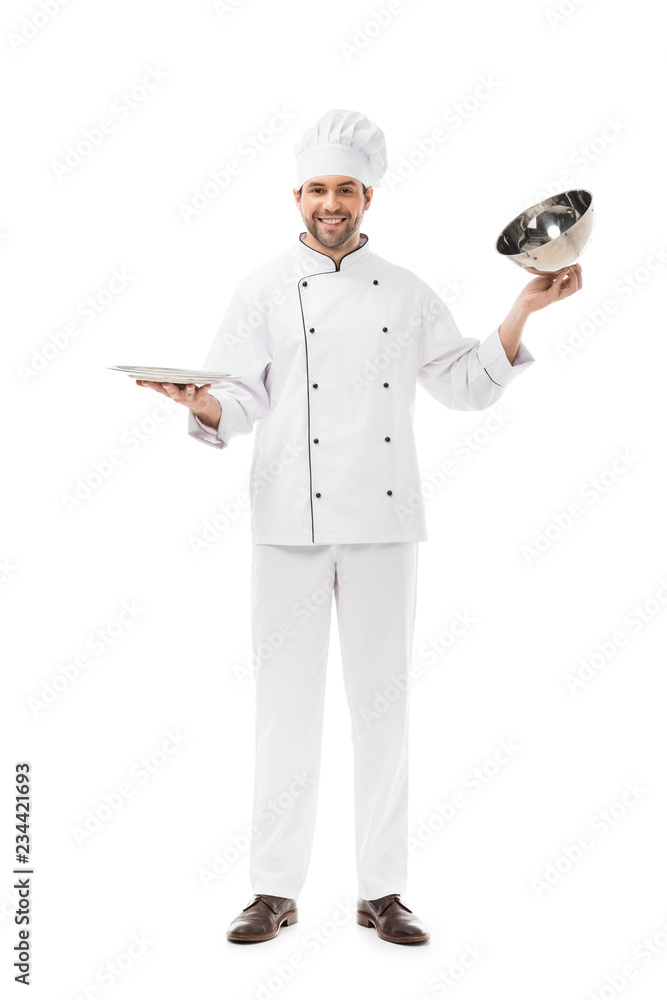 smiling young chef taking of serving dome from plate and looking at camera isolated on white