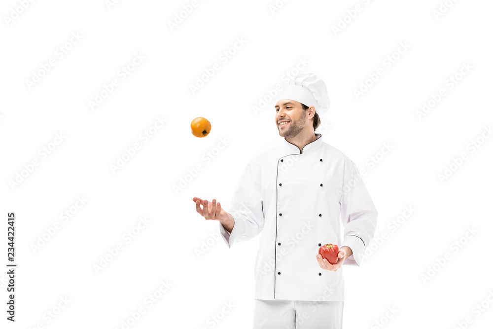 smiling young chef juggling with tomato and bell pepper isolated on white smiling young chef juggling with tomato and bell pepper isolated on white